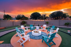 Un espace extérieur aménagé avec des chaises Adirondack et une table ronde, entouré d’un petit muret en briques et offrant une vue sur le coucher du soleil.