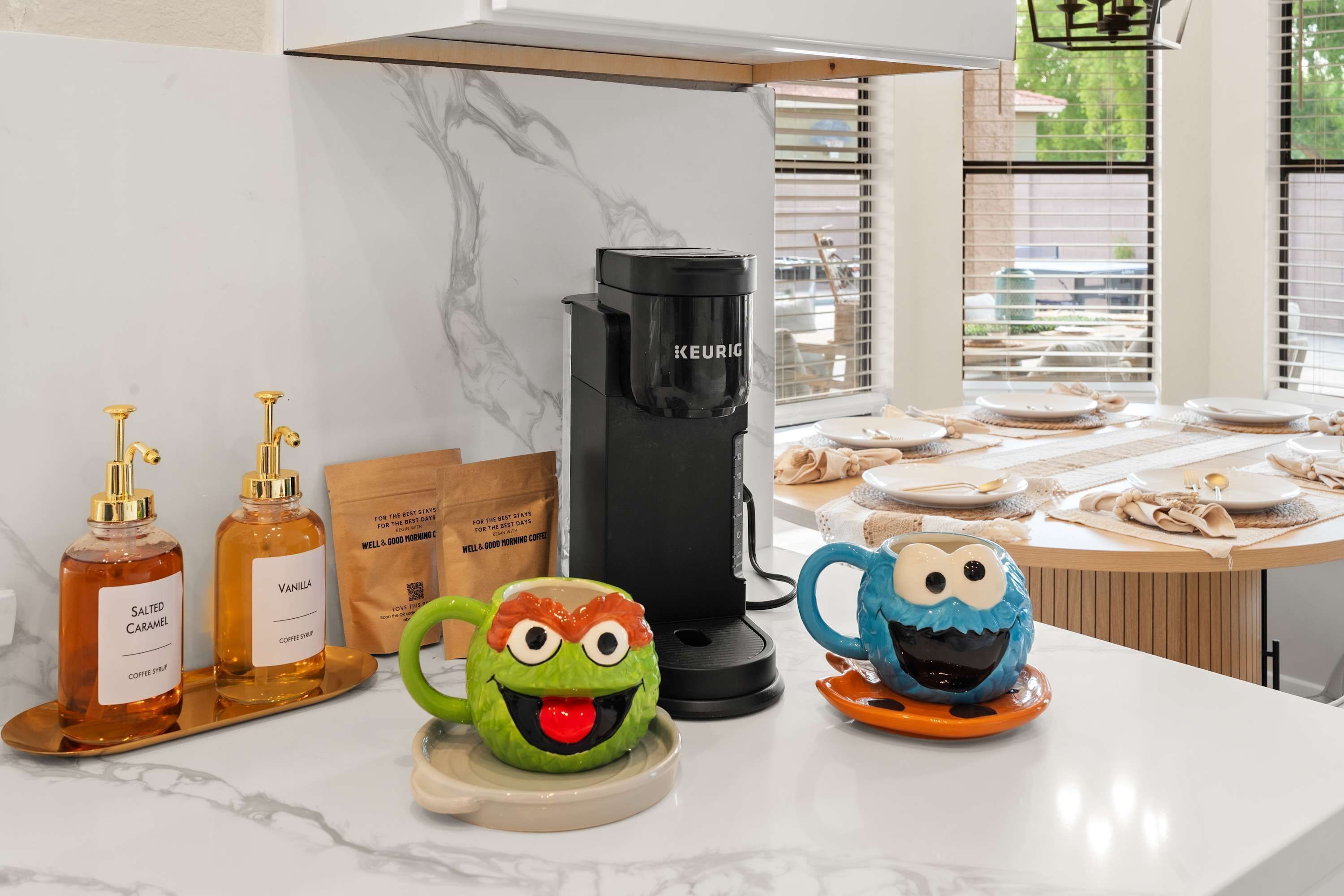Un coin café équipé d’une machine Keurig, de deux sirops pour café et de deux tasses en céramique décorées de motifs de dessins animés.