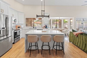 A modern kitchen with a central island, bar stools, and a dining area with a green sofa. - The Ultimate Stay Play Retreat 4BR Sleeps 13 (Chandler)