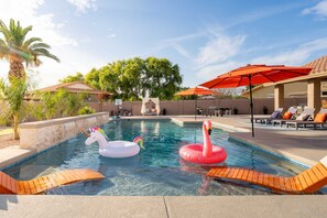 Une piscine avec deux bouées en forme de cygne gonflable, entourée de chaises longues et de parasols.