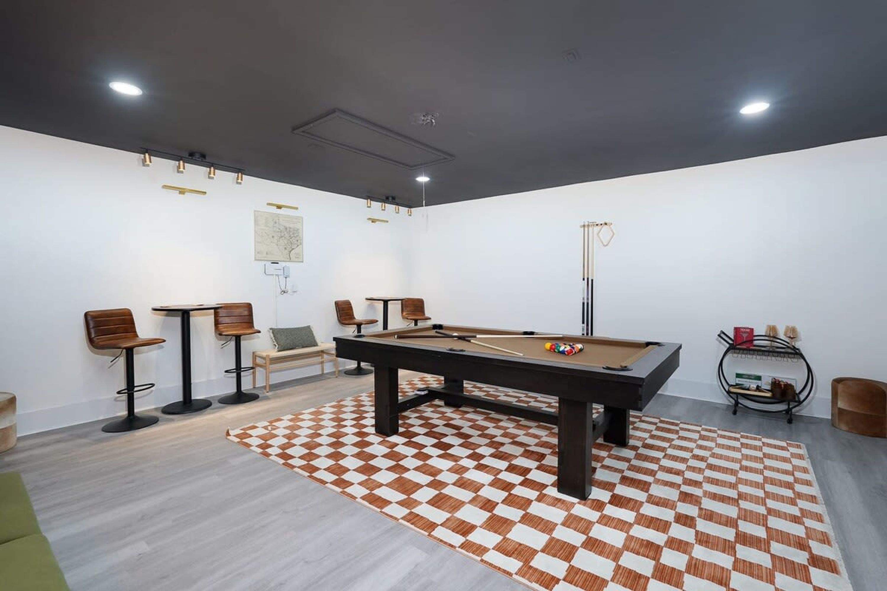 Una mesa de billar en una habitación con un tapete de cuadros, sillas y un mapa en la pared.