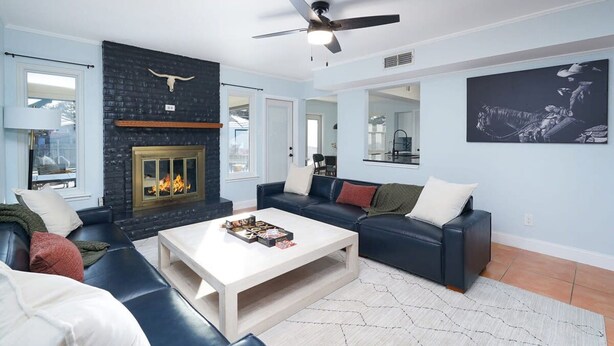 A living room with a fireplace, a ceiling fan, and a large painting on the wall. - Texas Tranquility Hot Tub Pool Putt Putt More (San Antonio)