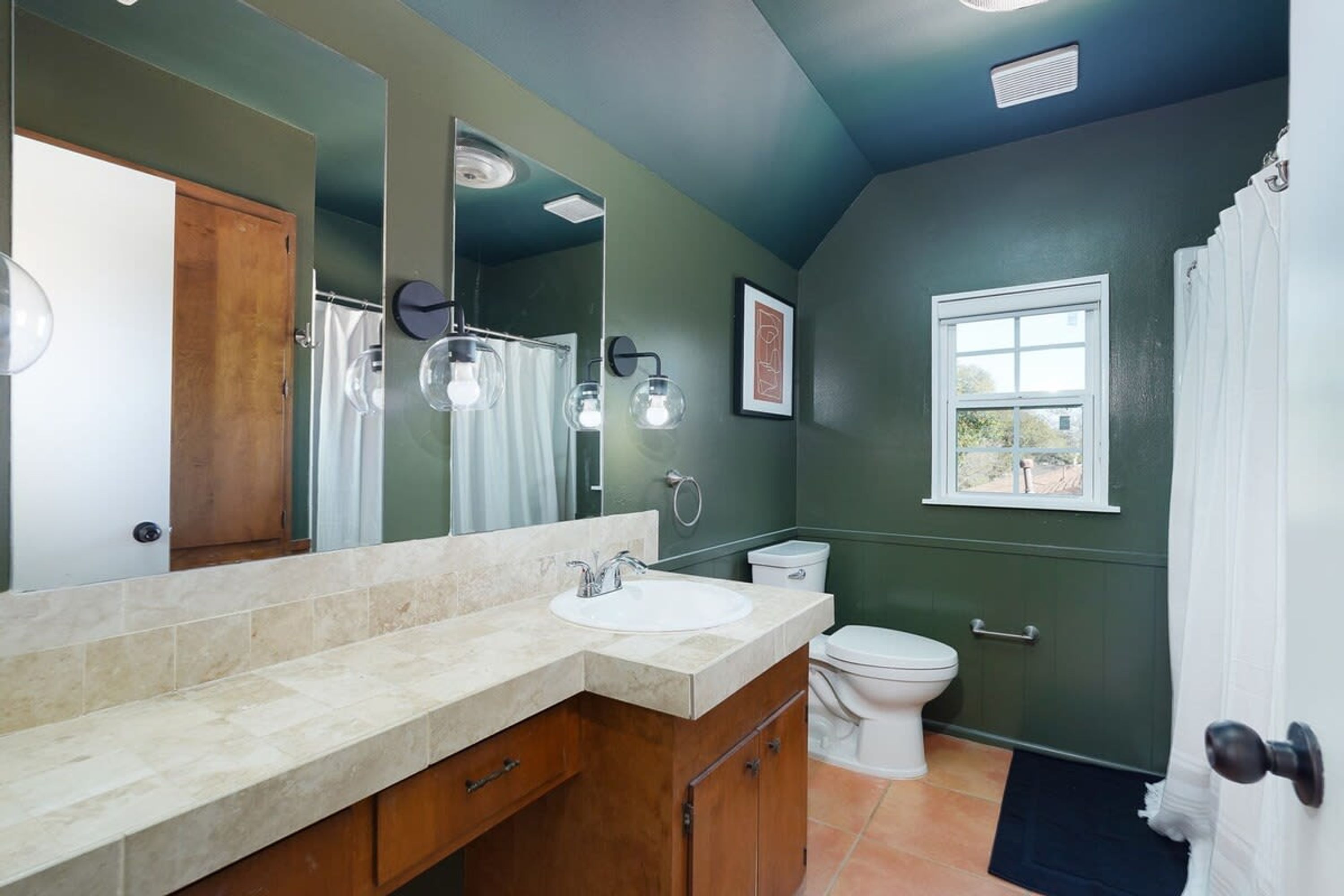 A bathroom with a large mirror, a sink, a toilet, and a shower area.