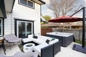 Eine Terrasse mit einem weißen Ecksofa, einem runden Tisch mit Feuerstelle und einem Whirlpool.