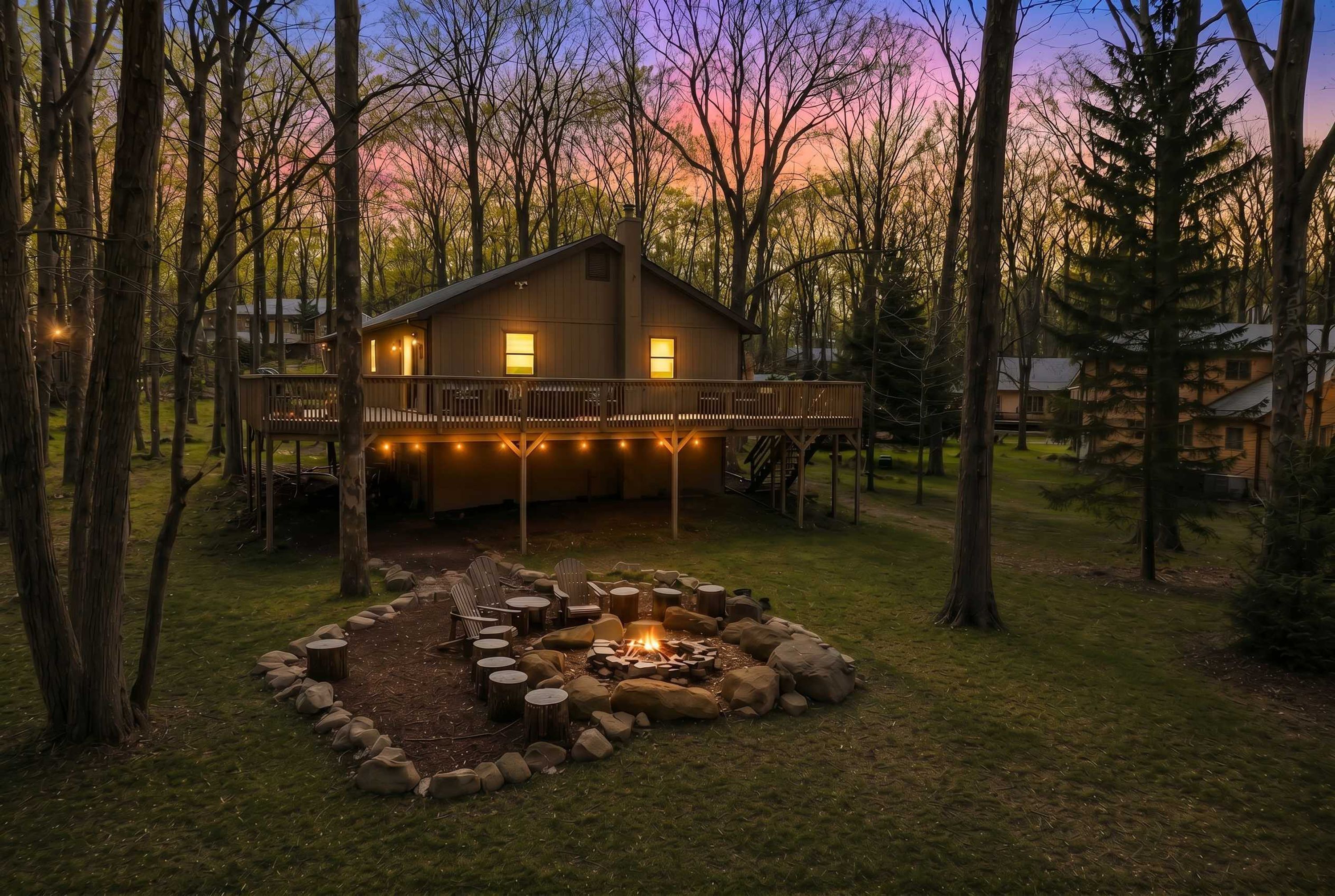 A cabin with a deck, a fire pit, and a surrounding wooded area.
