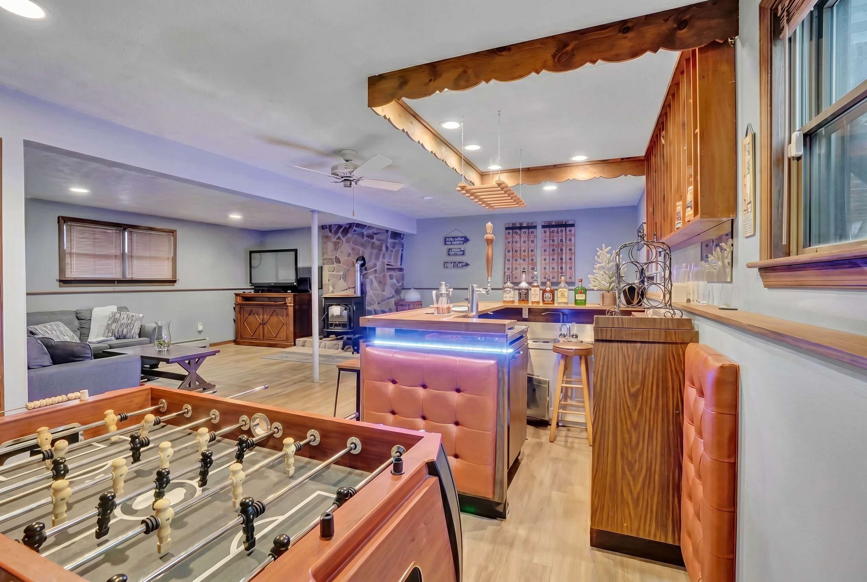 A modern living room with a foosball table, a stone wall, a bar area, and a seating area with a sofa and a television.