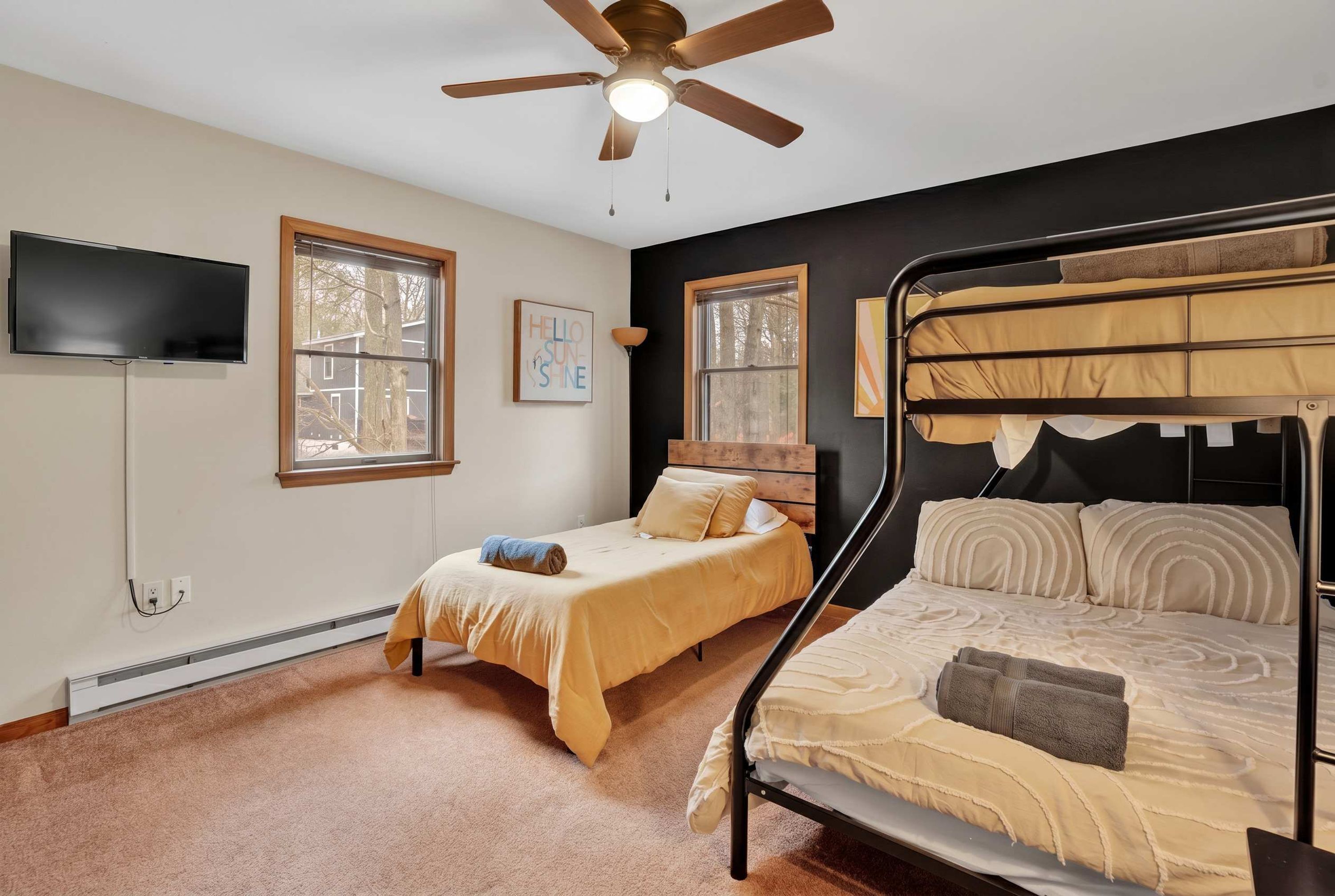 A bedroom with two beds, a ceiling fan, a TV, and windows.