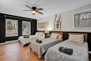 A room with two beds, a ceiling fan, and large windows with a forest view. - Poconos Retreat Hot Tub Firepits Sleeps 16 (Lake Harmony)