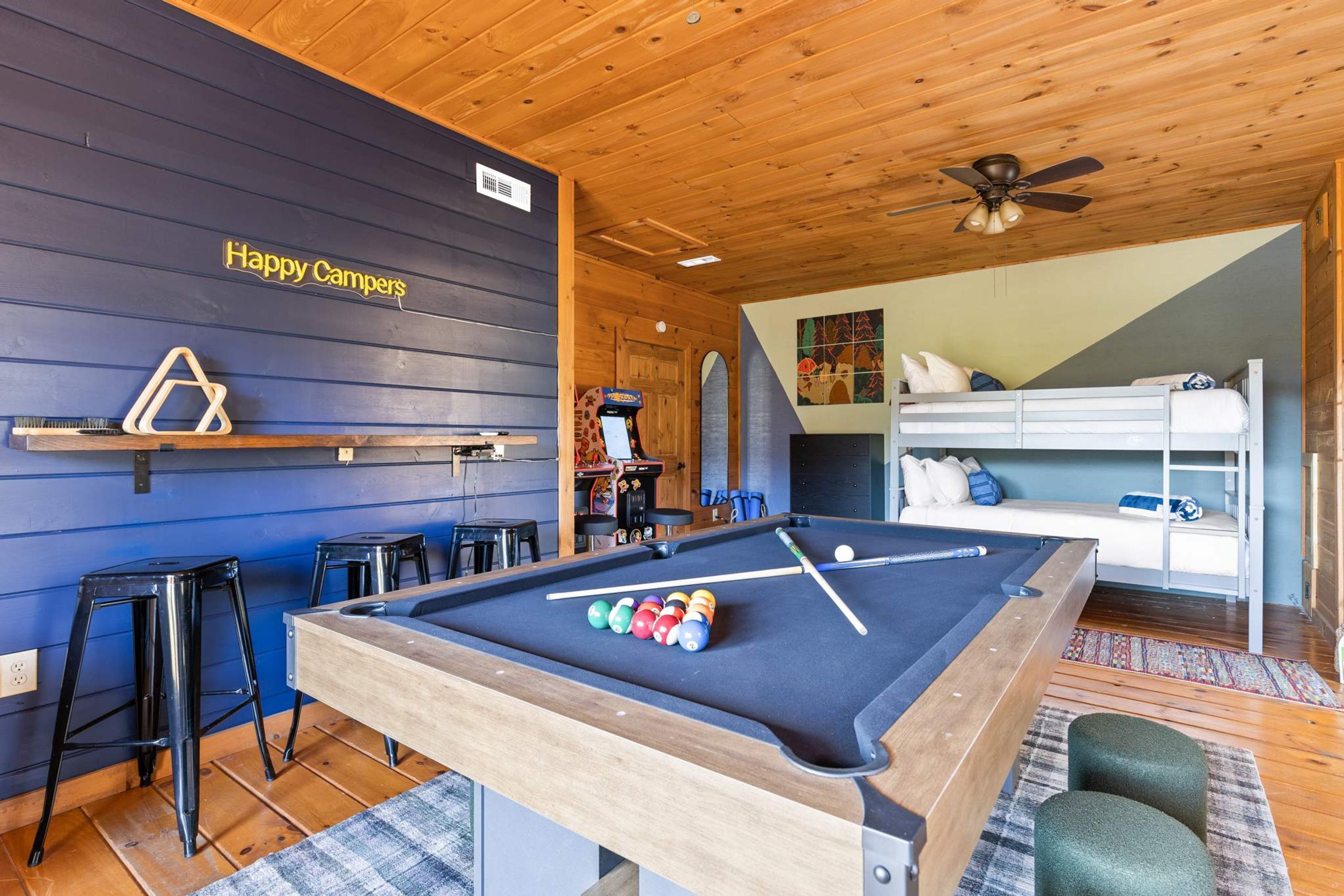 A pool table with balls, a ceiling fan, and a bunk bed in a room with wooden walls and a blue accent wall.