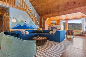 A cozy living room with a blue sofa, a wooden staircase, and a mountain mural on the wall. - Camp Wildgrove Hot Tub Sauna Mtn Views (Blue Ridge)