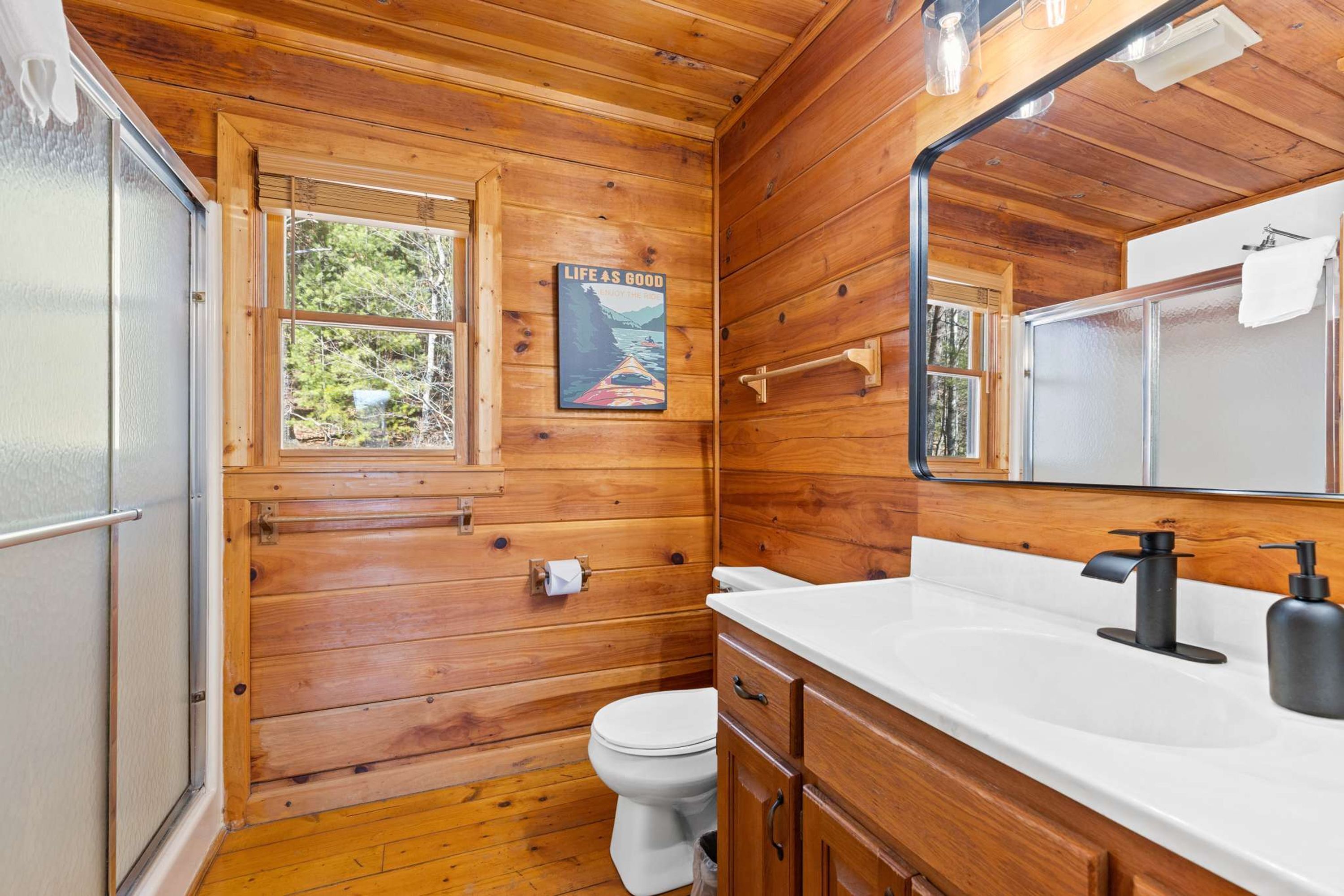A wooden cabin bathroom with a toilet, sink, and mirror.