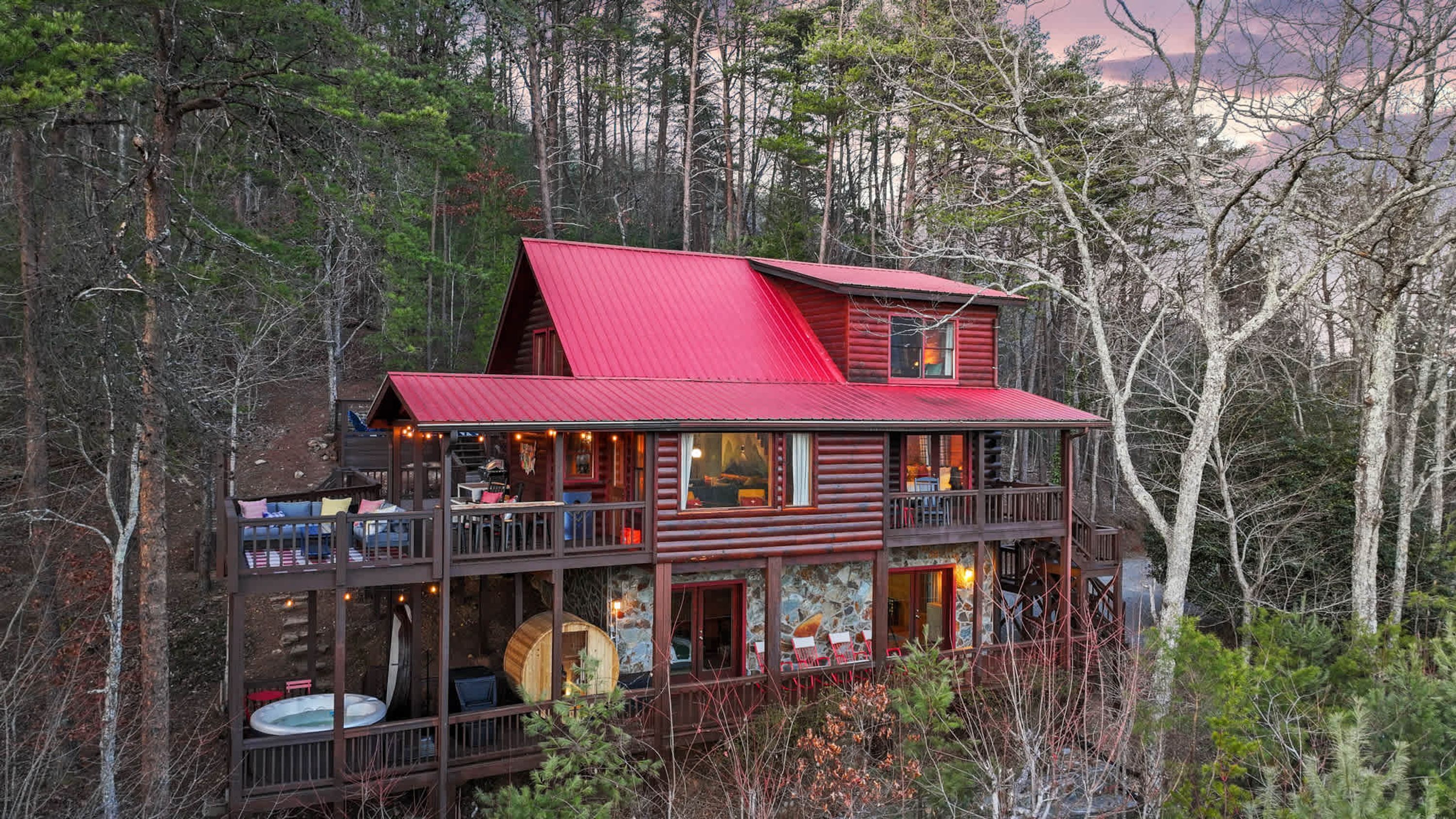 A two-story log cabin with a red roof, multiple decks, and a hot tub.