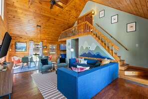 Un interior de cabaña acogedor con techo de madera, un sofá azul, un comedor y una escalera.