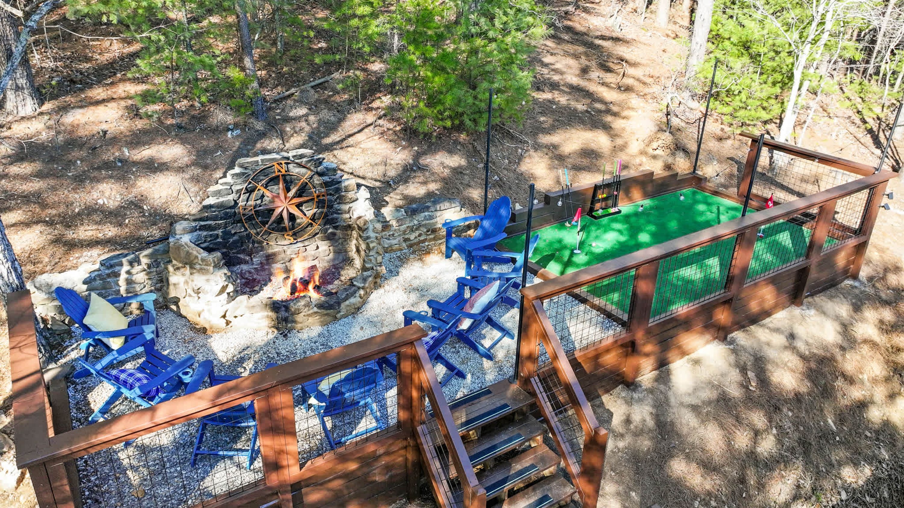 Eine Holzterrasse mit Feuerschale, Sitzgelegenheit im Freien und einem umzäunten Bereich mit grüner Rasenfläche.
