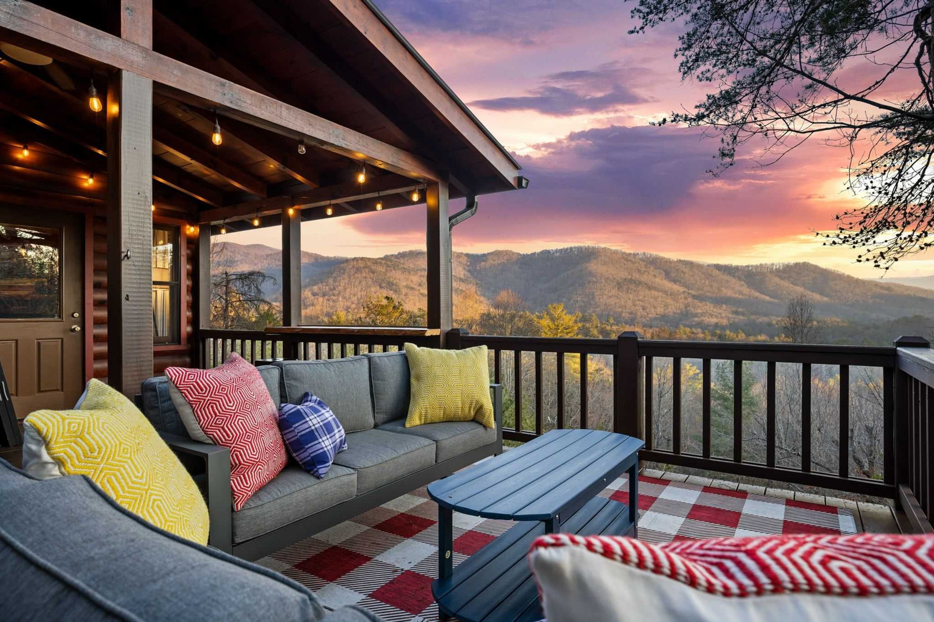 A covered outdoor seating area with a sofa and a table, overlooking a mountainous landscape.