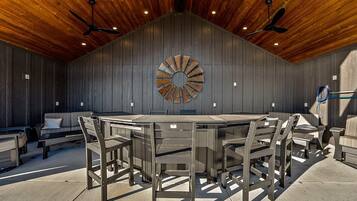 Un espacio de comedor al aire libre techado con mesa redonda y sillas, techo de madera y un adorno en la pared.