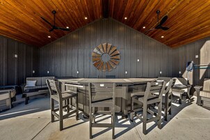 Un espacio de comedor al aire libre techado con mesa redonda y sillas, techo de madera y un adorno en la pared.