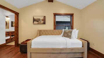 Un dormitorio con una cama grande, una ventana con persianas, un cuadro en la pared y suelo de madera.