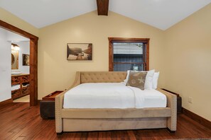 Un dormitorio con una cama grande, una ventana con persianas, un cuadro en la pared y suelo de madera.