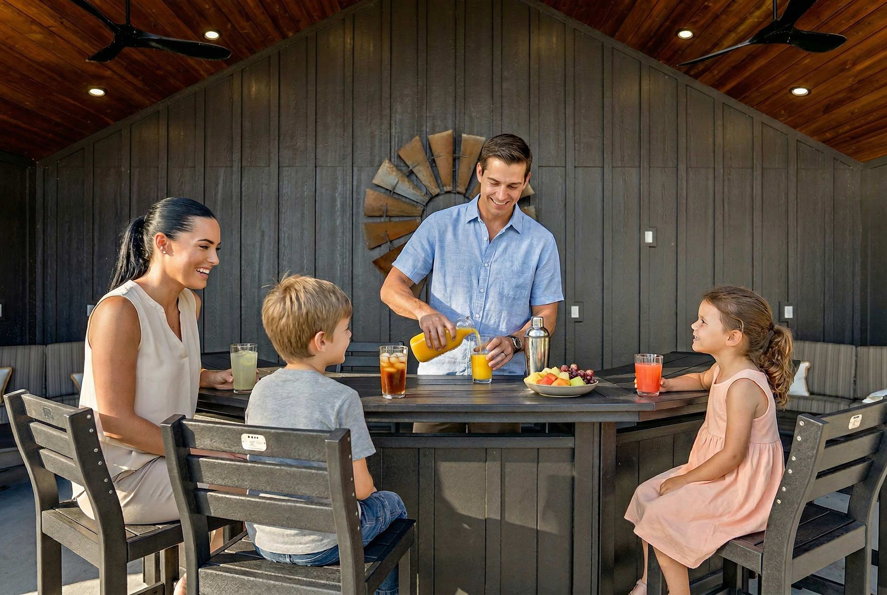 A family dining at an outdoor table with a modern design, surrounded by wooden chairs and a ceiling fan.