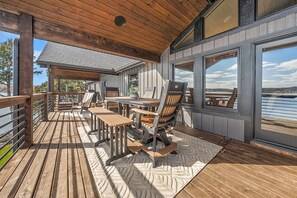 A wooden deck with outdoor seating and large windows overlooking a body of water. - Lakefront Oasis Private Dock Pool Sleeps 20 (Sunrise Beach)