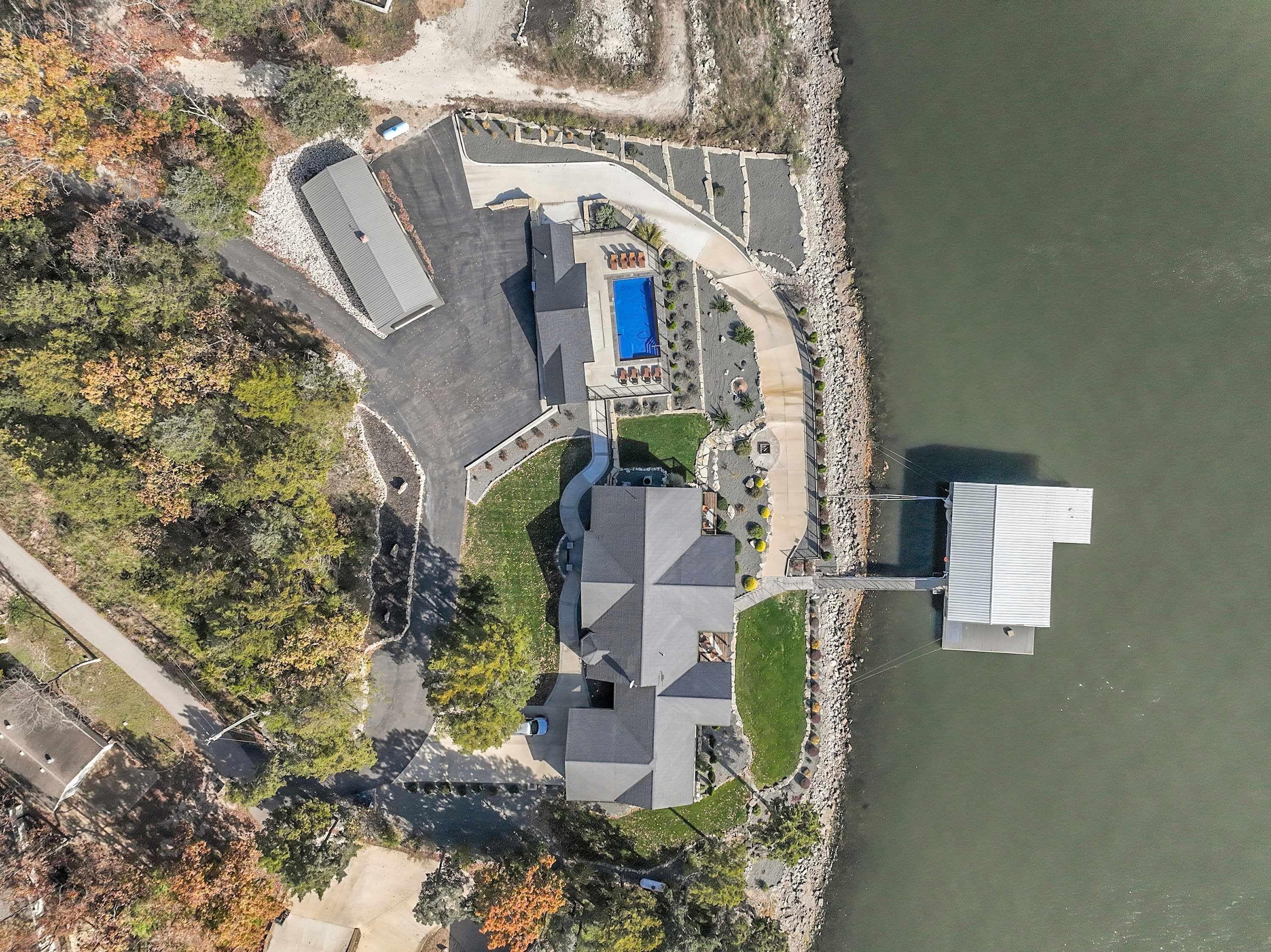 An aerial view of a property with a swimming pool, a parking area, and a dock extending into a body of water.