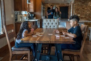 A dining area with a wooden table and chairs, a kitchen in the background, and a brick wall. - Lakefront Oasis Private Dock Pool Sleeps 20 (Sunrise Beach)