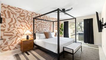 A four-poster bed with a bench, a bedside table, a lamp, and a patterned wall.