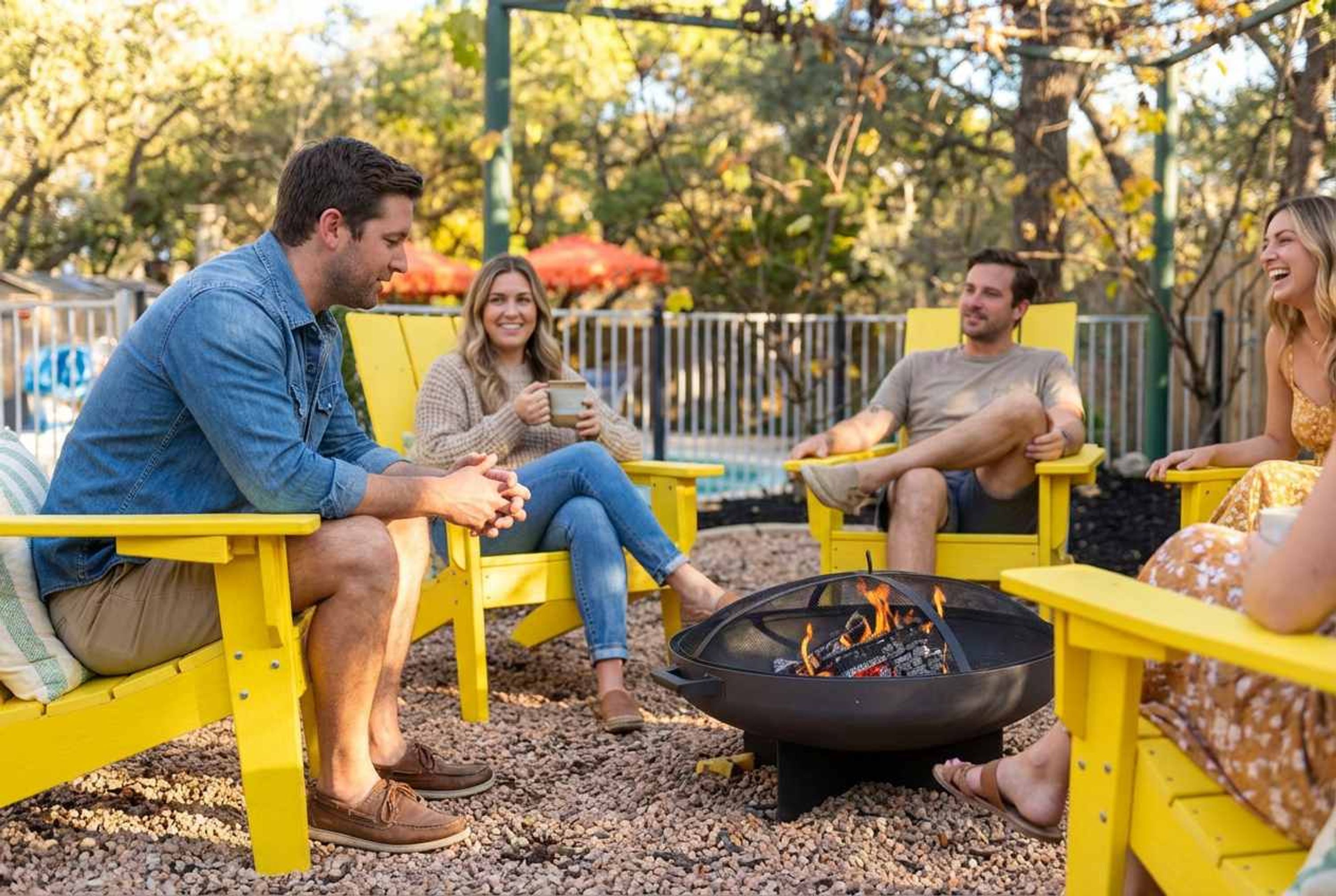 A group of people sitting on yellow chairs around a fire pit in an outdoor setting.