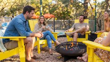 A group of people sitting on yellow chairs around a fire pit in an outdoor setting.