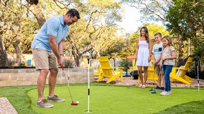 A family playing golf on a well-maintained lawn with a putting green and yellow chairs in the background. - Sleeps 14 Pool Hot Tub Near Airport (San Antonio)