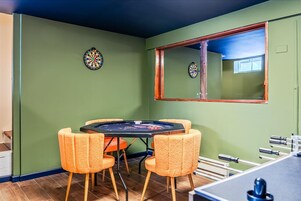 Una habitación con dardos, una mesa con sillas y una ventana con espejo.
