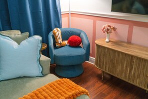 A room with a blue armchair, a wooden sideboard, and a television mounted on the wall. - Austin Encore Pool Hot Tub Putt-putt (Austin)