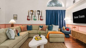 A living room with a sectional sofa, a coffee table, a TV, and guitars on the wall. - Austin Encore Pool Hot Tub Putt-putt (Austin)