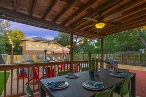 An outdoor patio with a table set for four, surrounded by chairs, a ceiling fan, and string lights. - Austin Encore Pool Hot Tub Putt-putt (Austin)