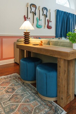 A room with a wooden table, blue ottomans, a patterned rug, and guitars on the wall. - Austin Encore Pool Hot Tub Putt-putt (Austin)