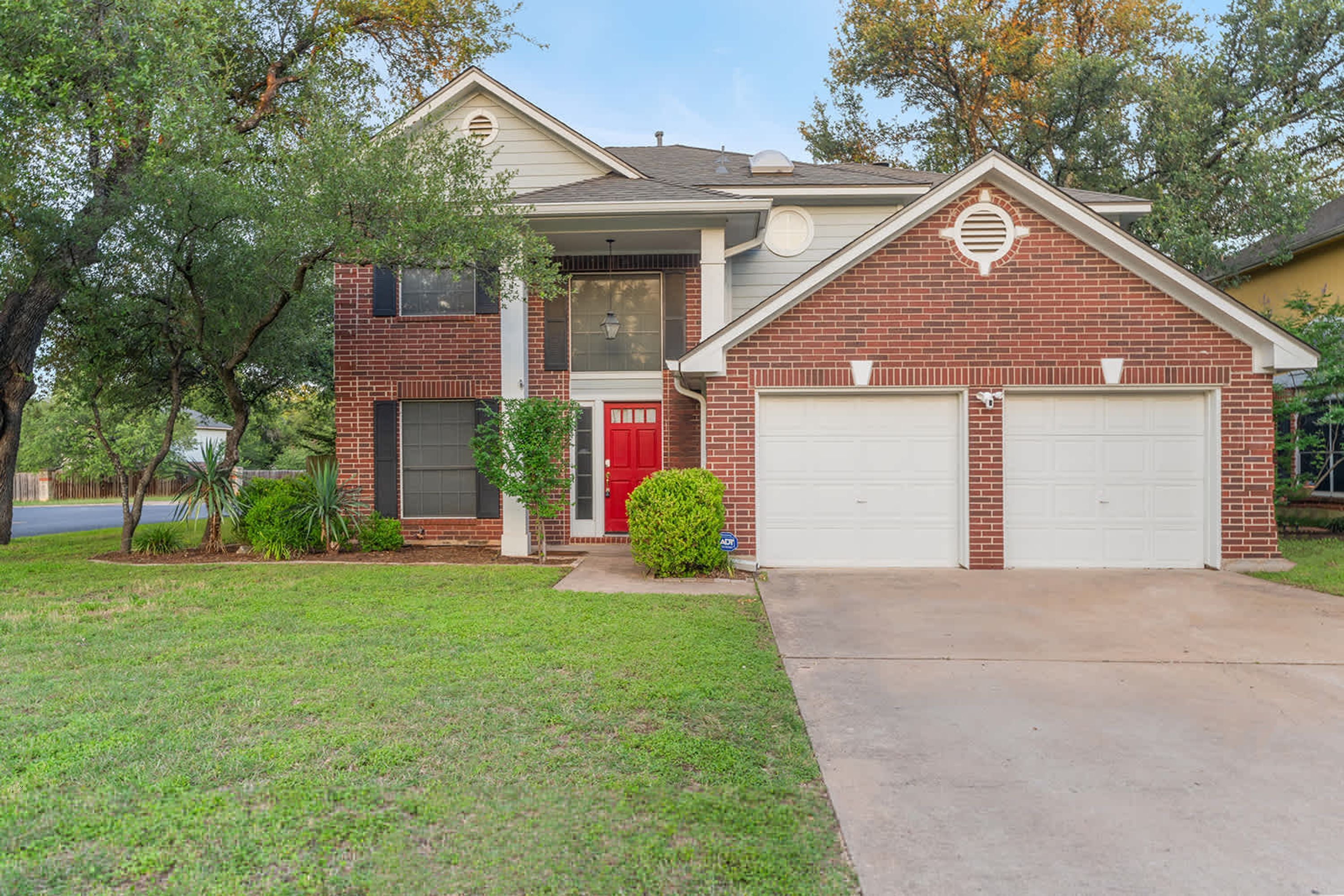 A two-story house with a red door, a garage, and a well-maintained lawn.