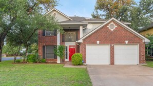 A two-story house with a red door, a garage, and a well-maintained lawn. - Austin Encore Pool Hot Tub Putt-putt (Austin)