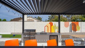 Eine Terrassenausstattung im Freien mit einem Grill, orangefarbenen Stühlen und einem Wandgemälde.