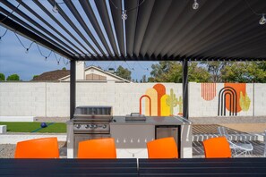 Eine Terrassenausstattung im Freien mit einem Grill, orangefarbenen Stühlen und einem Wandgemälde.