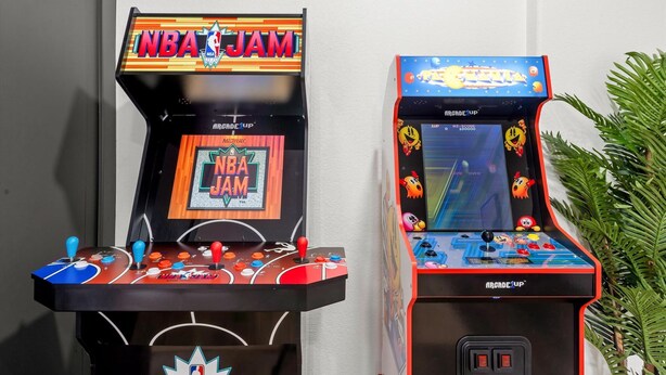 Zwei Spielautomaten, einer beschriftet mit 'NBA JAM' und der andere mit 'PAC-MATTA', beide mit Joysticks und farbenfroher Grafik.