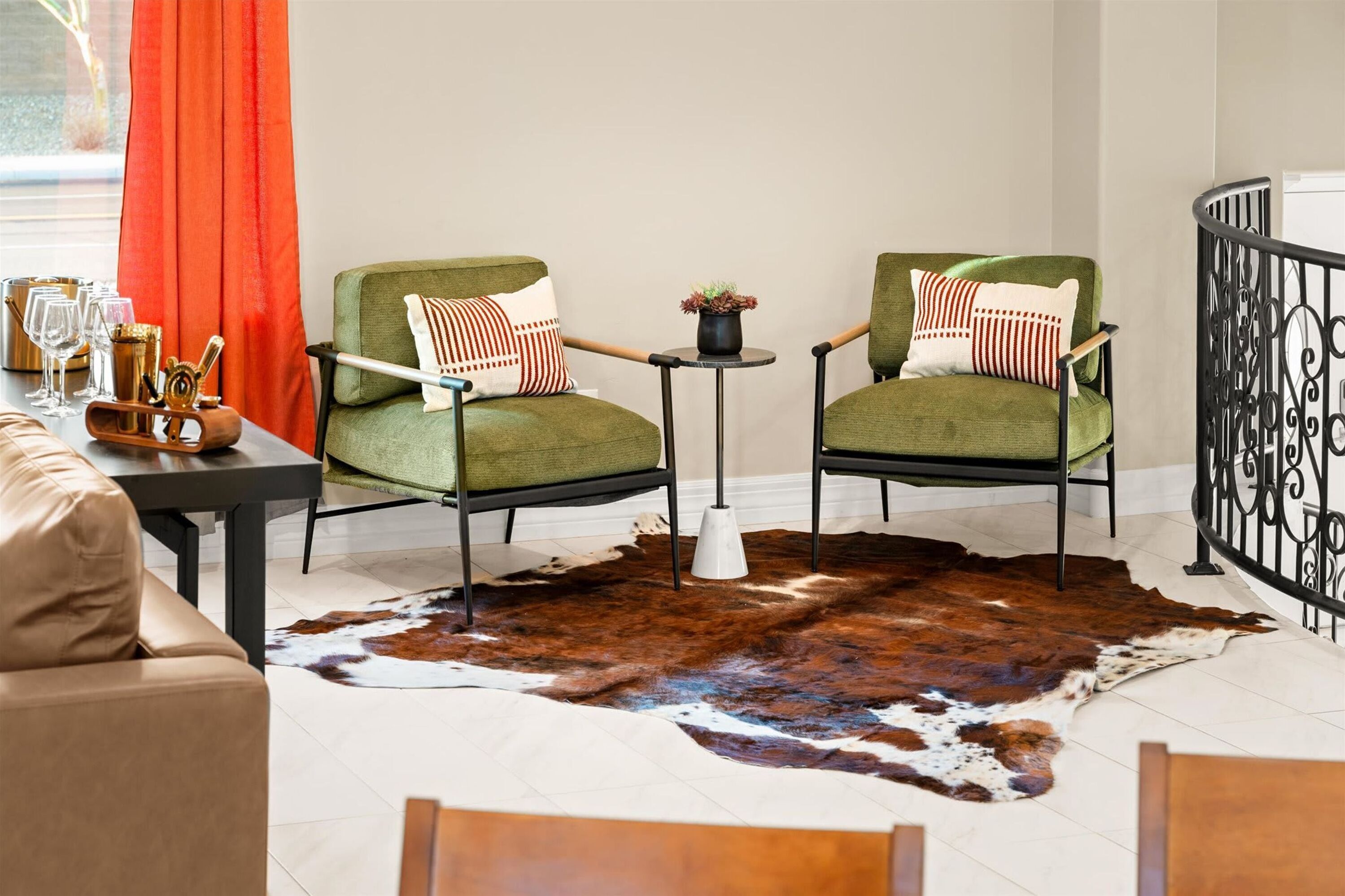 A room with two green upholstered chairs, a small round table, a cowhide rug, and a leather sofa.