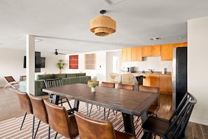 Une cuisine moderne avec des meubles en bois, un coin repas doté d’une grande table et de chaises, et un ventilateur de plafond.