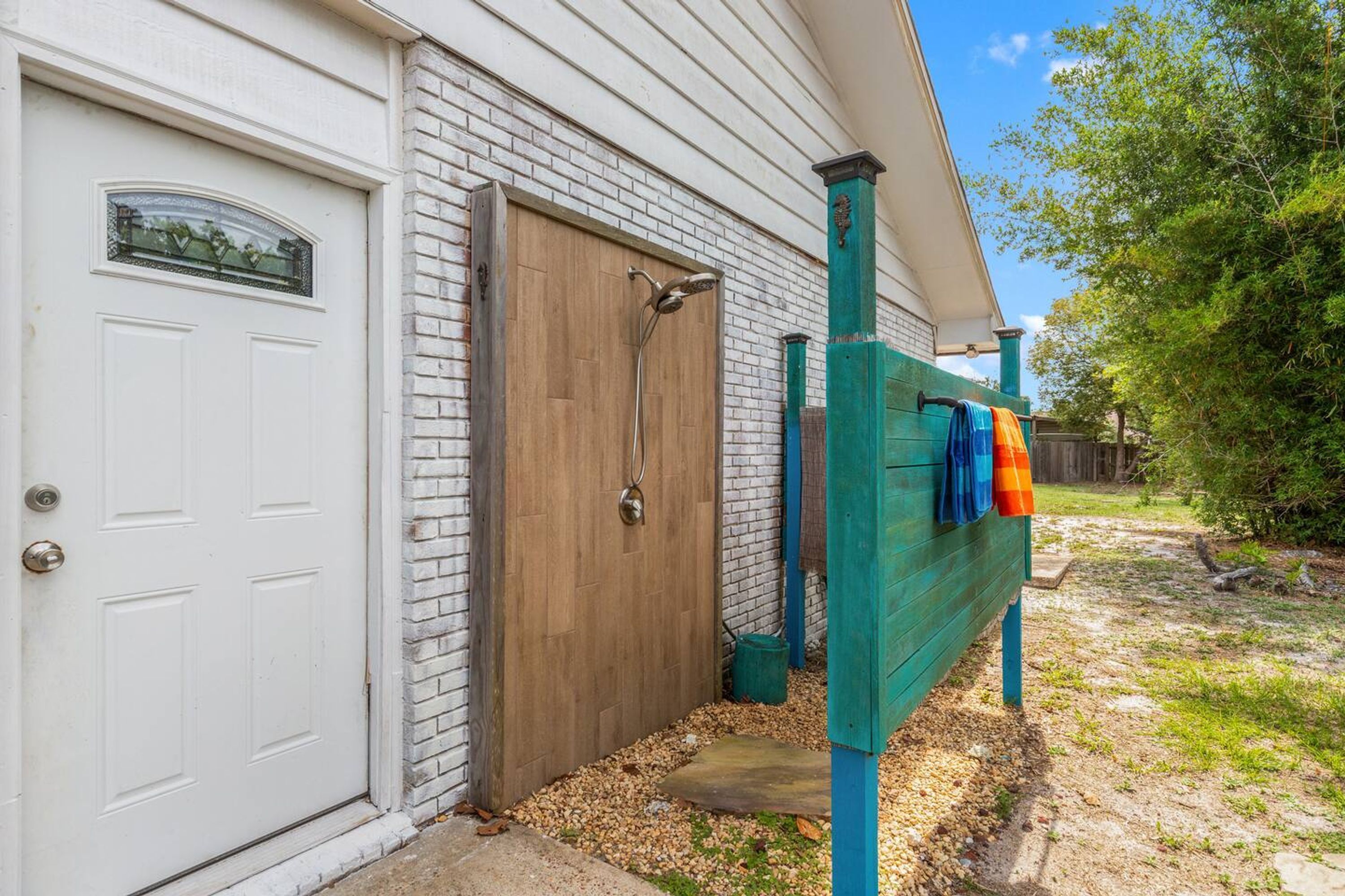 Een wit huis met een houten garage deur, een metalen deur en een groene hek met kleurrijke handdoeken eraan.