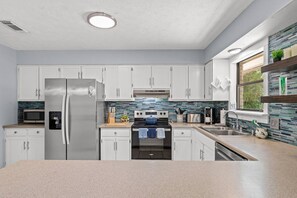 Cozinha moderna com armários brancos, eletrodomésticos de aço inoxidável e backsplash com azulejos azuis e verdes.