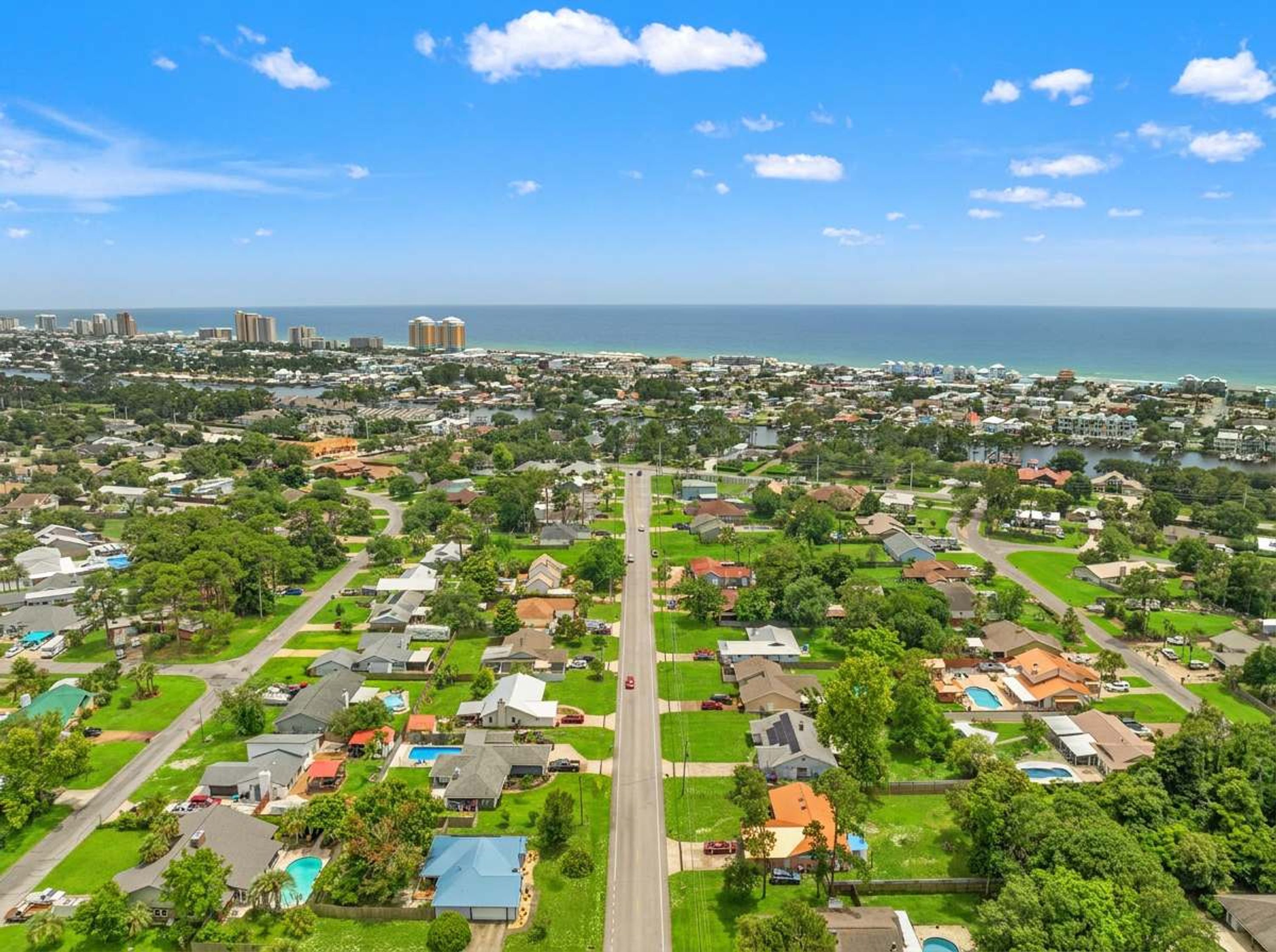 A residential area with houses, green lawns, and a clear view of the ocean.