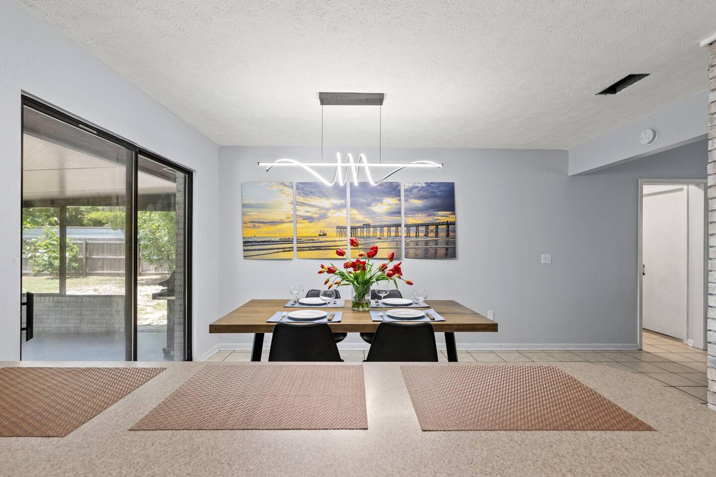 A modern dining area with a wooden table, black chairs, and a vase of red flowers.