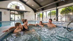 A family enjoying a hot tub in a well-lit indoor pool area with large windows and a high ceiling. - Beach Front 7th Floor Views Pools Hot Tub (Orange Beach)