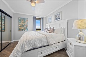 A bedroom with a bed, a nightstand, a ceiling fan, and artwork on the walls. - Beach Front 7th Floor Views Pools Hot Tub (Orange Beach)