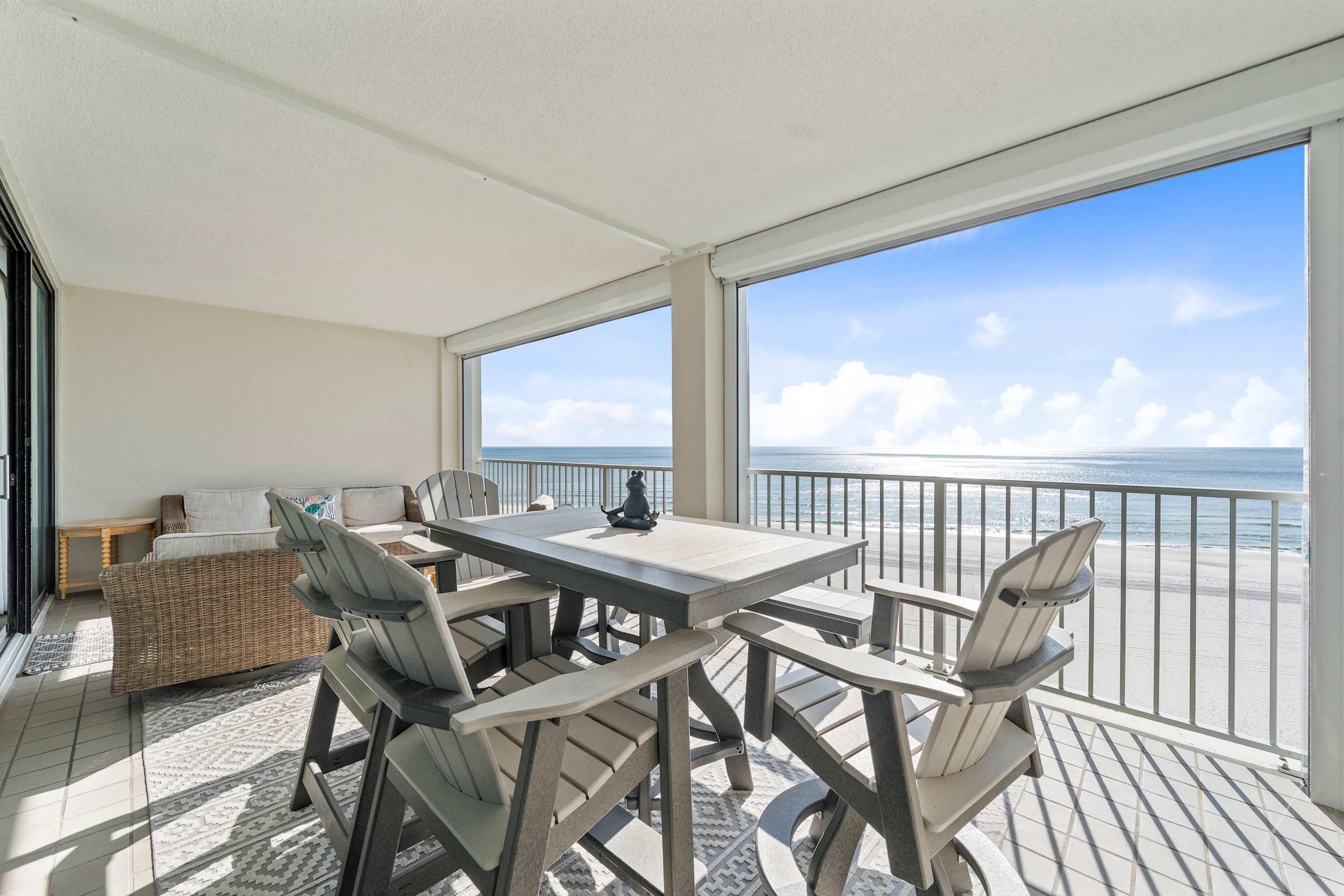 A covered outdoor area with a table and chairs, a wicker sofa, and a view of the ocean.